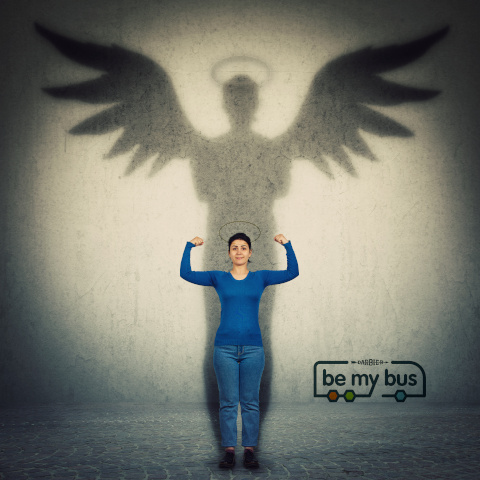 Casual confident woman flexing arm muscles as casting a hero shadow with angel wings on a dark room wall. Super power, inner strength ambition and leadership. Female independence and energy concept.